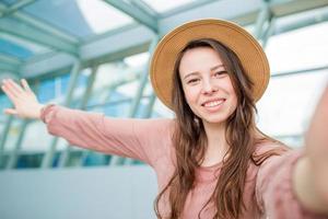 jeune femme prenant un selfie dans le salon de l'aéroport en attente d'embarquement à l'aéroport international photo