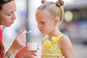 jeune mère et ses filles mangeant des glaces à l'extérieur. maman nourrit sa fille de glaces dans la rue photo