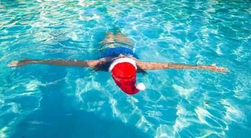 vue arrière de la belle femme en bonnet de noel sur l'eau bleue photo