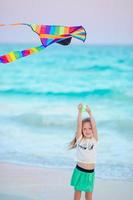 petite fille en cours d'exécution avec cerf-volant sur la plage tropicale. enfant joue sur le rivage de l'océan. enfant avec des jouets de plage. photo