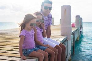 famille de trois personnes assises sur un quai en bois bénéficiant d'une vue sur l'océan photo