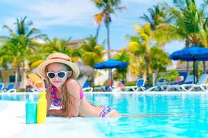 petite fille avec une bouteille de crème solaire dans la piscine photo