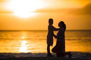 petite fille et silhouette de mère heureuse au coucher du soleil à la plage photo