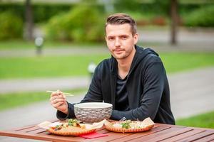 jeune homme mangeant des nouilles à emporter dans la rue photo