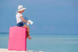petite fille de touristes avec une grosse valise sur une plage blanche tropicale