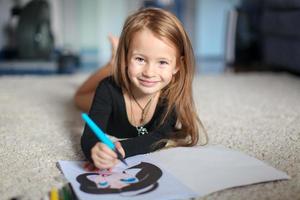 portrait d'une douce charmante jeune fille qui dessine avec son coloriage à la maison photo