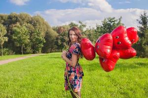 jeune femme séduisante en belle robe avec des ballons rouges marchant dehors photo