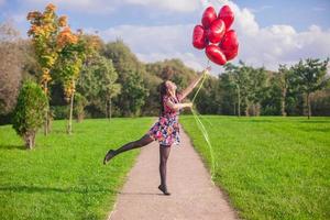 jeune fille heureuse en robe colorée s'amuser avec des ballons rouges à l'extérieur photo