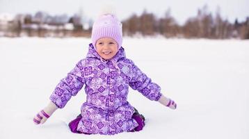 heureuse adorable fille s'amusant sur la neige à la journée ensoleillée d'hiver photo