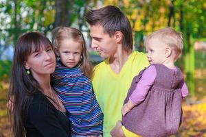 portrait d'une jeune famille charmante avec deux kida profitant du temps qu'il fait dans le parc d'automne jaune photo