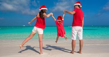 famille heureuse de trois personnes en chapeaux de noël pendant les vacances tropicales photo