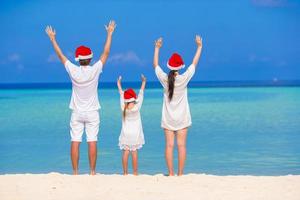famille heureuse de trois personnes en chapeaux de père noël pendant les vacances tropicales photo