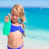 petite fille adorable en maillot de bain avec une bouteille de lotion solaire photo