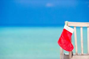 chaussette de père noël sur chaise près de la plage tropicale avec eau de mer turquoise et sable blanc. concept de vacances de noël photo