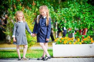 deux jolies petites filles souriantes posant devant leur école. adorables petits enfants très excités à l'idée de retourner à l'école photo