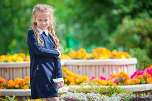 jolie petite fille souriante posant devant son école le premier septembre. adorable petit enfant très excité à l'idée de retourner à l'école photo