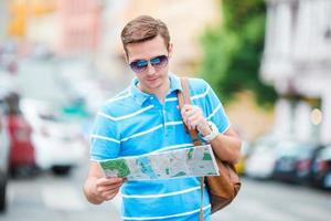 jeune touriste caucasien avec un plan de la ville et un sac à dos en europe. mec heureux en regardant la carte de la ville européenne à la recherche d'attractions. photo