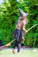 adorable petite fille portant un costume de sorcière avec un balai s'amusant à l'halloween photo