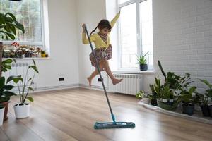 une fille danse avec une vadrouille pour nettoyer le sol dans une nouvelle maison - nettoyage général dans une pièce vide, la joie de déménager, aide aux tâches ménagères photo