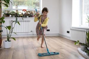 une fille danse avec une vadrouille pour nettoyer le sol dans une nouvelle maison - nettoyage général dans une pièce vide, la joie de déménager, aide aux tâches ménagères photo