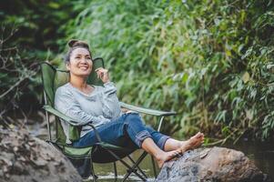 jeune femme assise sur une chaise de camping en ruisseau pour se détendre photo