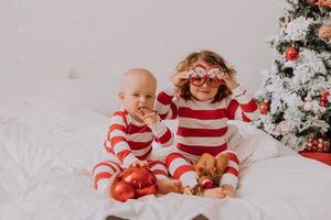 les enfants en pyjama rouge et blanc mangent des bonbons de noël assis dans leur lit. frère et sœur, garçon et fille partagent des cadeaux. Matin de noël. mode de vie. espace pour le texte. photo de haute qualité
