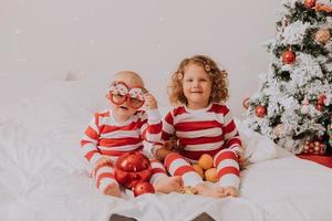 les enfants en pyjama rouge et blanc mangent des bonbons de noël assis dans leur lit. frère et sœur, garçon et fille partagent des cadeaux. Matin de noël. mode de vie. espace pour le texte. photo de haute qualité
