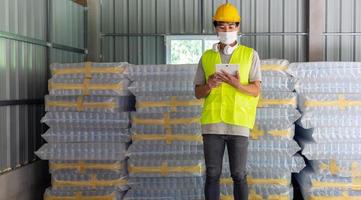 travailleur asiatique vérifiant le stock de bouteilles en plastique dans l'entrepôt et comparant le numéro d'équilibrage dans le système après l'expédition de la livraison. utiliser une tablette pour mettre à jour le stock en ligne photo