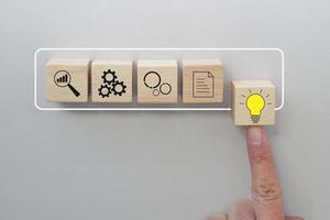 doigt poussant le cube en bois avec le symbole de l'ampoule sur le bloc rectangle infographique virtuel. concept progressif d'entreprise vers le succès. photo