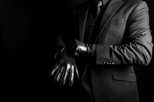 portrait d'homme en costume sombre tirant sur des gants en cuir sur fond noir. concept de gangster ou de tueur à gages mafieux. photo