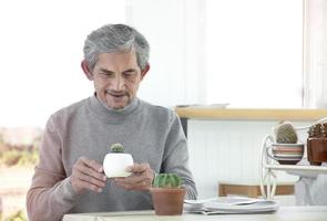 Portrait d'un homme asiatique senior âgé assis près d'une fenêtre en verre le matin pour travailler à domicile et vérifier ses affaires sur son ordinateur portable sur la table avec une mise au point sérieuse, douce et sélective. photo