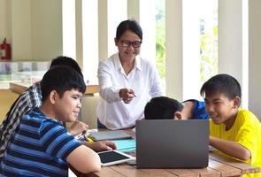 jeunes adolescents asiatiques et enseignant, ils sont en classe, les élèves font une feuille de travail et écoutent ses conseils sur le projet scolaire, un adulte aide les enfants à faire le concept de projet scolaire. photo