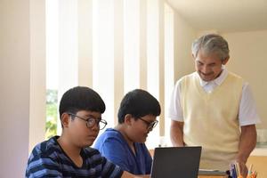 enseignant âgé asiatique et jeunes adolescents entourant l'intérieur de la salle pour consulter et faire le travail du projet scolaire, enseignant âgé aide les enfants à résoudre les problèmes et les conseille pour obtenir une bonne note. photo