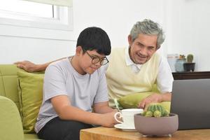 grand-père senior asiatique et son fils passent du temps ensemble à la maison pour connecter un casque avec son ordinateur portable pour regarder et jouer à des jeux en ligne, mise au point douce et sélective, élever le concept des adolescents. photo