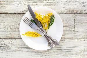 Assiette de table de fête avec fourchette et couteau et décoration de fleurs de mimosa sur fond de bois blanc avec espace de copie photo