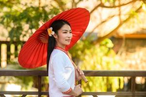 femme asiatique portant une robe thaïlandaise typique avec un parapluie rouge., costume thaïlandais photo