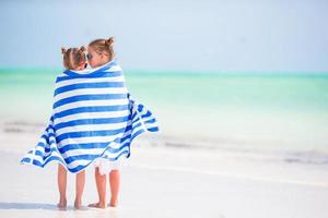 petites filles mignonnes enveloppées dans une serviette à la plage tropicale. enfants en vacances à la plage photo