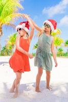 petites filles adorables en chapeaux de père noël pendant les vacances à la plage s'amuser ensemble photo