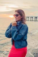 portrait de mode en plein air d'une fille élégante portant des lunettes de soleil à la mode et une veste en jean sur la plage. photo