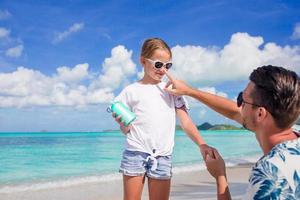 jeune père appliquant de la crème solaire au nez de sa fille sur la plage. protection solaire photo