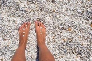 gros plan sur des jambes de femmes avec des cailloux sur une plage de sable blanc photo