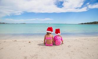 petites filles mignonnes en chapeaux de père noël s'amusant sur une plage exotique photo