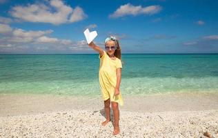 adorable petite fille avec un avion en papier dans les mains sur la plage de sable blanc photo