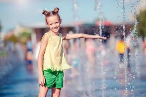 petite fille adorable s'amuser dans la fontaine de la rue lors d'une chaude journée ensoleillée photo