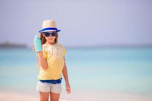 petite fille adorable avec une bouteille de lotion solaire sur la plage photo