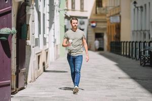 heureux jeune homme urbain buvant du café dans la ville européenne à l'extérieur photo