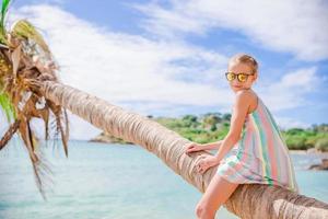 adorable petite fille assise sur un palmier pendant les vacances d'été sur la plage blanche photo