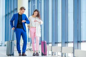 couple avec bagages à l'aéroport international se dépêchant de prendre un vol pour atterrir. homme et femme regardant leur horloge à l'intérieur près d'une grande fenêtre photo