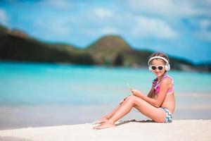 petite fille adorable sur la plage écoutant la musique dans de gros écouteurs photo