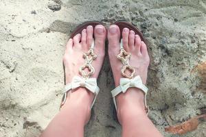 gros plan de tongs lumineuses et de jambes sur du sable blanc photo